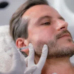 A close-up of a man reclining while a gloved practitioner administers an injection into his jaw, demonstrating the procedure used in Botox for teeth grinding.