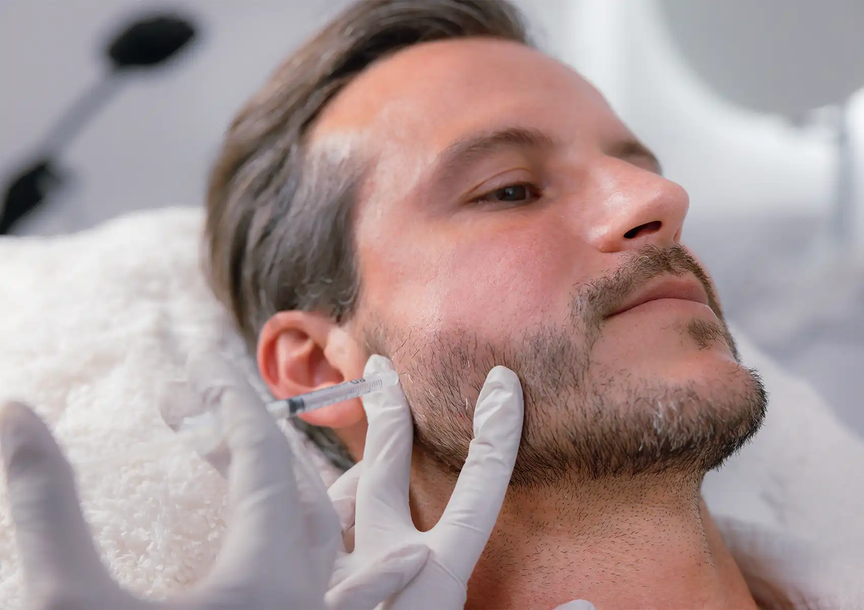 A close-up of a man reclining while a gloved practitioner administers an injection into his jaw, demonstrating the procedure used in Botox for teeth grinding.