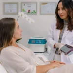A professional in a white coat presenting a dermal filler product box to a seated female patient during a consultation at a beauty clinic bali.