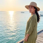 A woman wearing a sun hat on a wooden pier by the ocean, illustrating sun exposure that often prompts skin treatments at a beauty clinic bali.