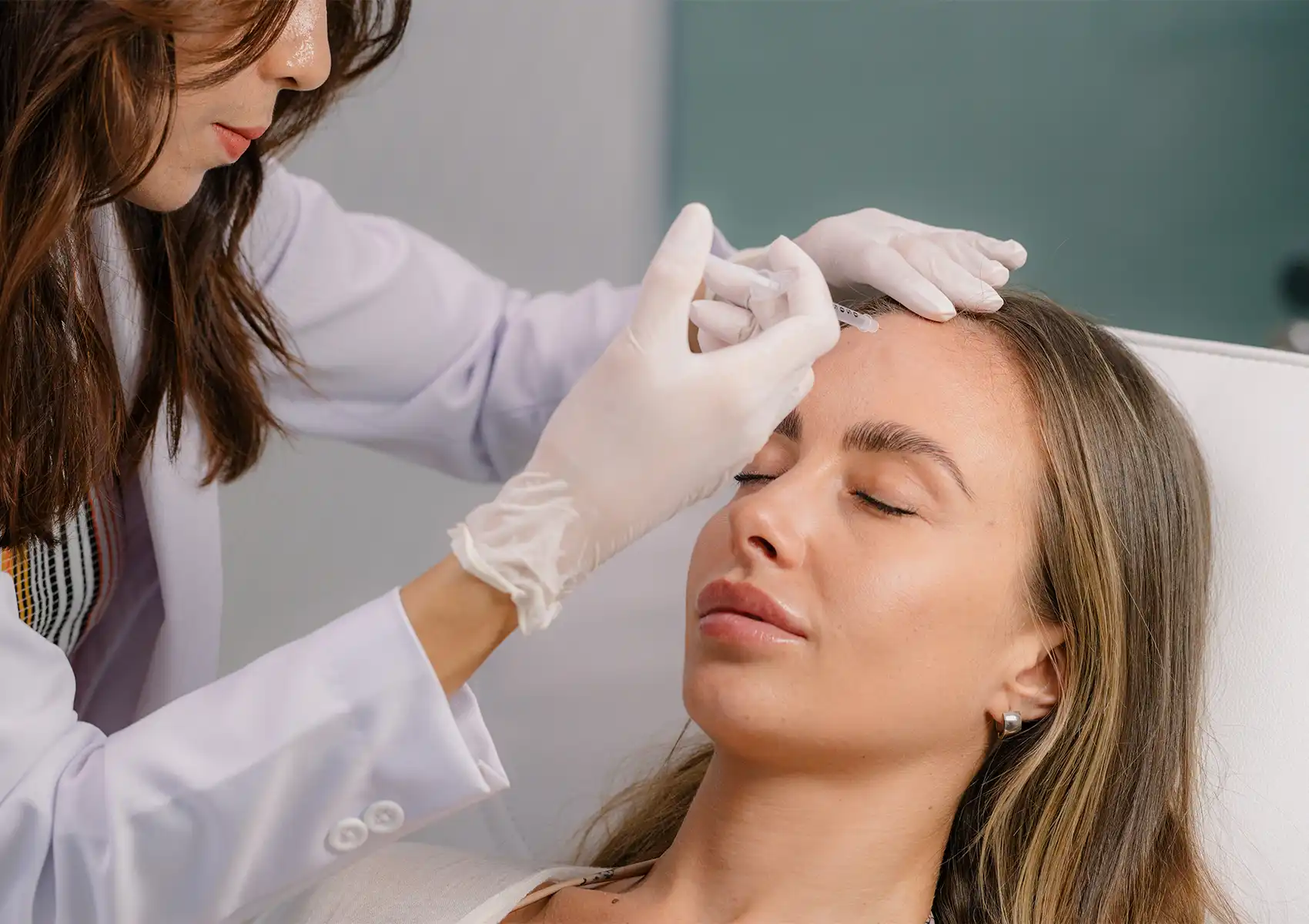 A medical professional in a white coat administering a cosmetic injection to a relaxed female patient's forehead at a beauty clinic bali.