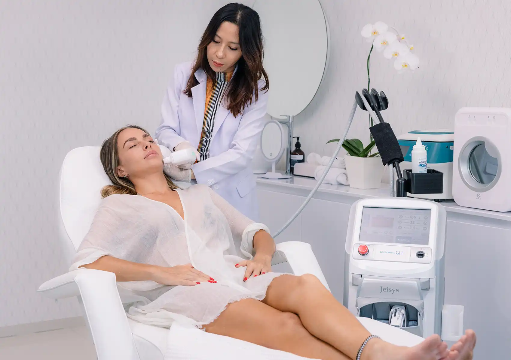 A practitioner in a white lab coat applies a handheld Jeisys ultrasound device to a reclining patient's jawline at a beauty clinic Bali.