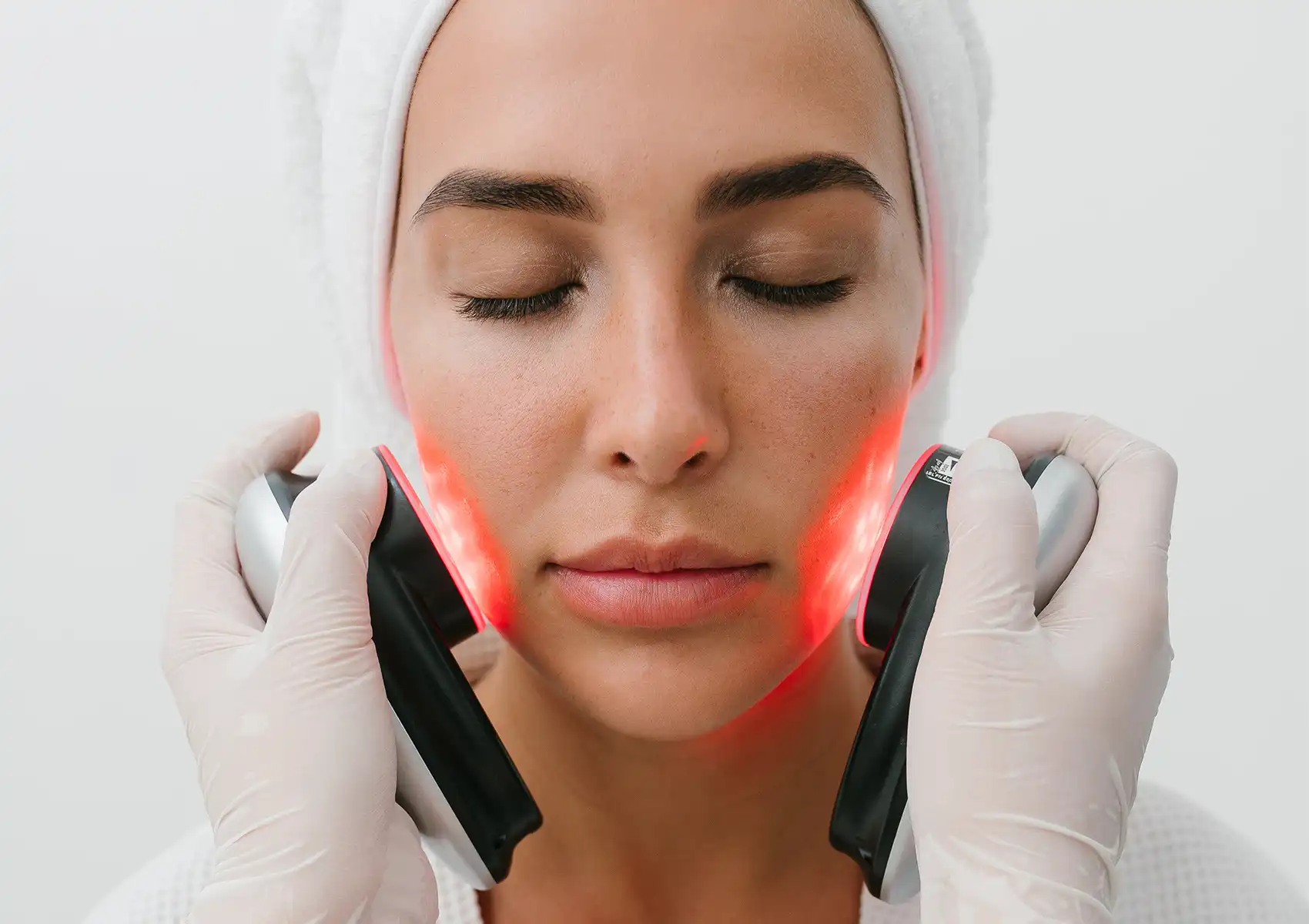 A woman with her eyes closed receiving red LED light therapy on her cheeks from a gloved professional at a beauty clinic bali.
