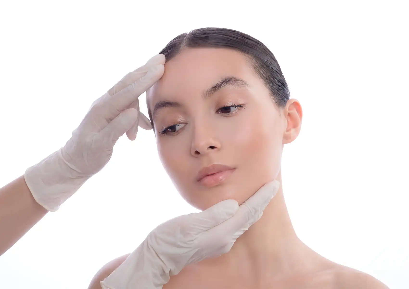 Gloved hands of a medical professional gently examining a woman's facial structure and skin condition during a consultation at a beauty clinic bali.
