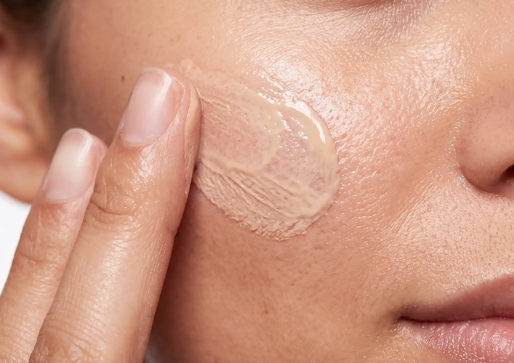 A close-up of a finger applying skincare cream to a person's cheek, representing topical solutions often recommended by a beauty clinic bali.