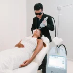 A male practitioner wearing protective glasses uses a specialized laser device on a relaxed female patient's face in a modern beauty clinic bali.