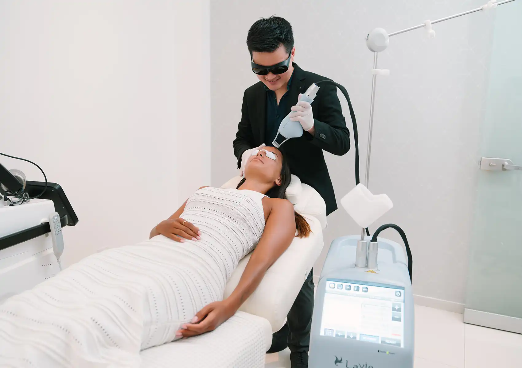 A male practitioner wearing protective glasses uses a specialized laser device on a relaxed female patient's face in a modern beauty clinic bali.