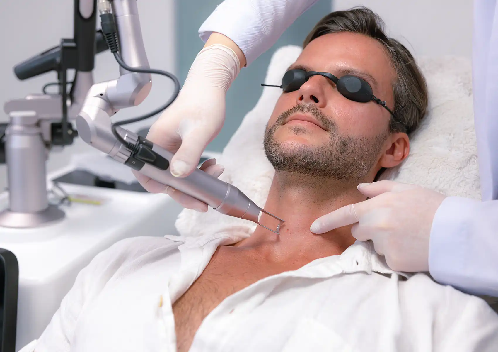A close-up view of a practitioner targeting a spot on a male patient's neck with a Pico laser device while the patient wears protective eyewear during a session at a beauty clinic bali.