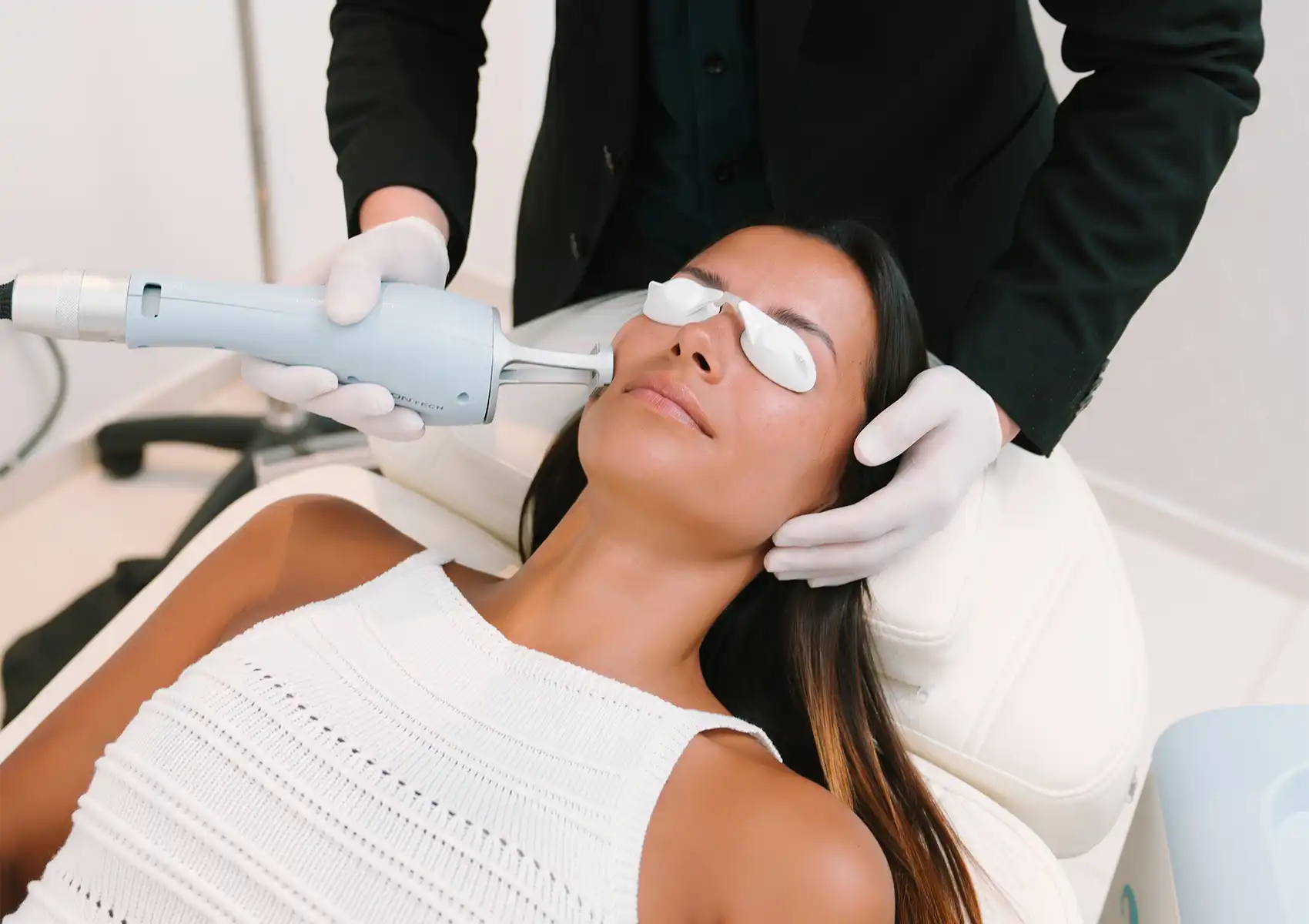 A close-up view of a practitioner's gloved hands applying a laser treatment device to a patient's cheek while she wears protective eye shields at a beauty clinic bali.