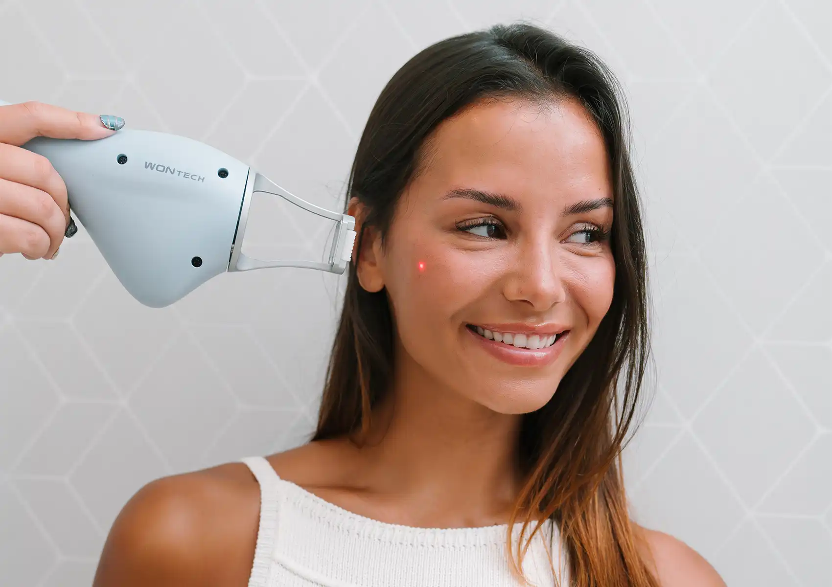 A smiling woman receives a targeted laser treatment on her cheek, with a small red dot visible from the WONTECH device, during a skincare session at a beauty clinic bali.